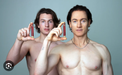 Bryan Johnson and another shirtless man against a pale blue background, holding their fingers in frame shapes